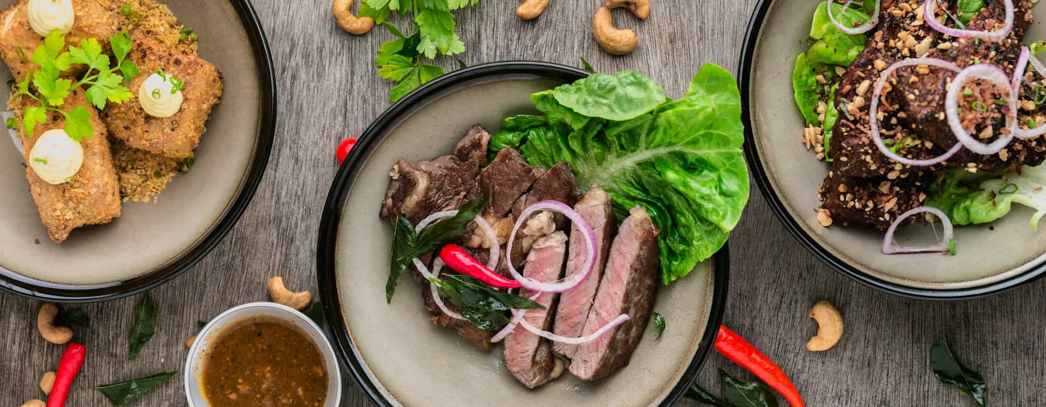 Three white bowls with black rims, each filled with a meat and salad dish
