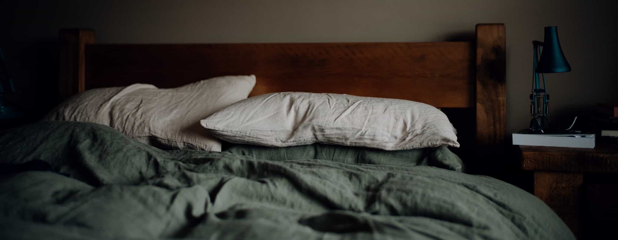 A messy un-made bed in a dark room.