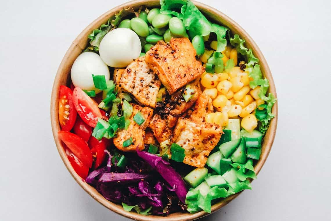 A salad bowl with lettuce, red onion, sweetcorn, chicken, edamame, tomato and cucumber