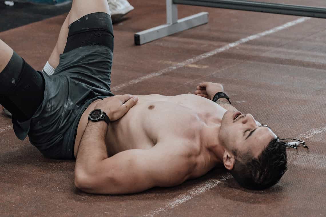 A man wearing shorts lying on a running track and looking exhausted.